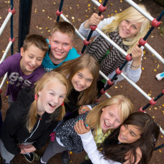 A group of smiling schoolchildren posing by a jungle gym.