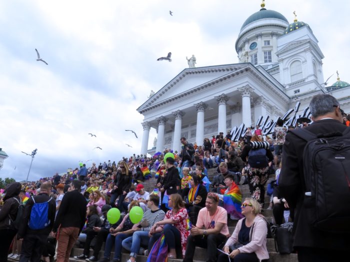 A large crowd of people sitting on the stairs of Helsinki cathedral.