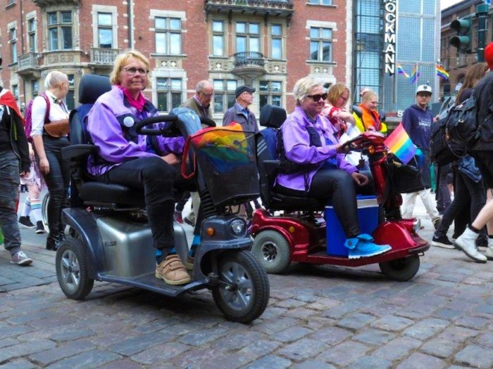 Two elderly people participating in the parade on their senior scooters.