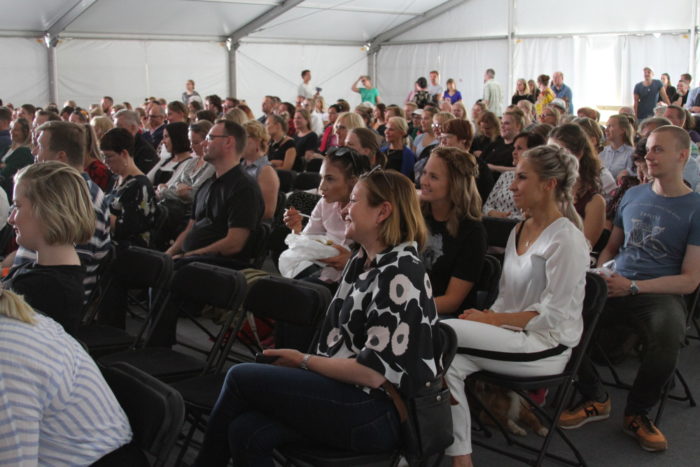 A large crowd sitting on chairs inside a white tent.