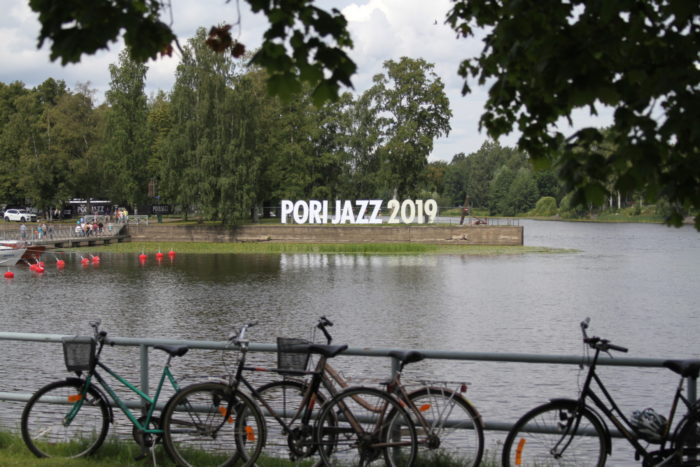 A riverbank with bicycles; Pori Jazz 2019 sign on the opposite bank.