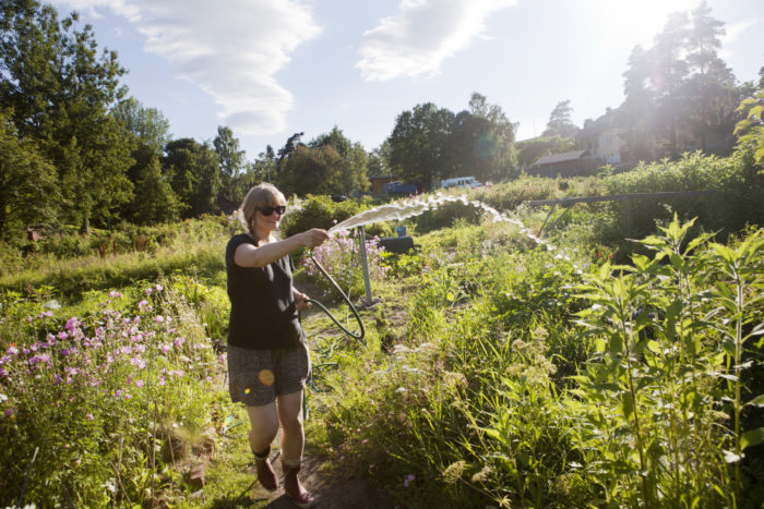 A smiling woman waters plants at a community garden.