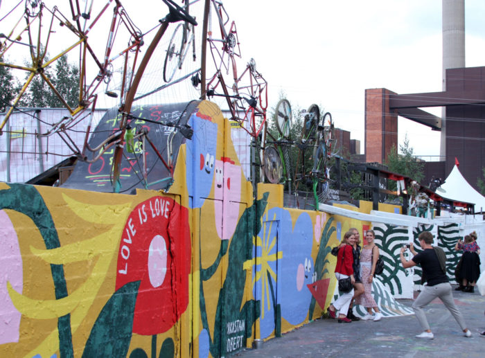 People take photos in front of a wall of artwork.