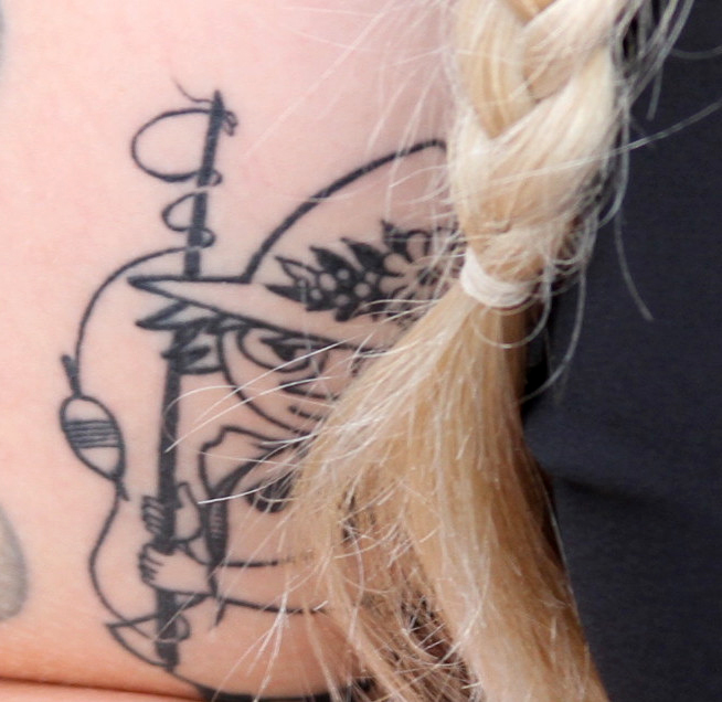 A tattoo of the Moomin character Snufkin is visible behind a blond hair braid.