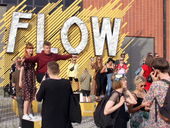 People pose for photos in front of a big sign that says Flow.