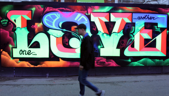 A festival-goer walks past a big and colourful work of graffiti that says Love.