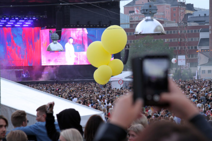 A large crowd gathers to watch Alma on stage.