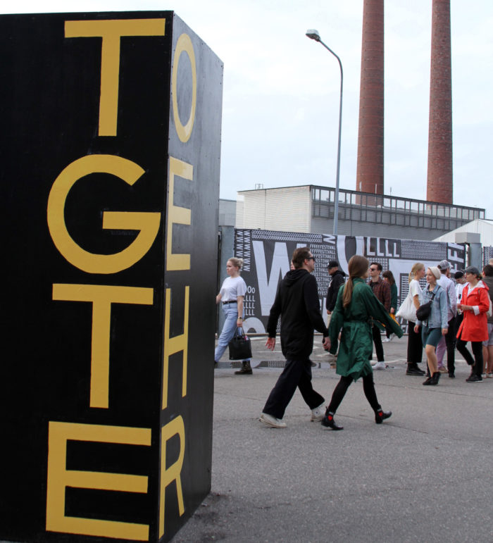 Festival-goers walk past a work of street art that says Together.