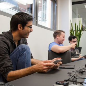 A group of people sit in a conference room looking at their phones and tablets.