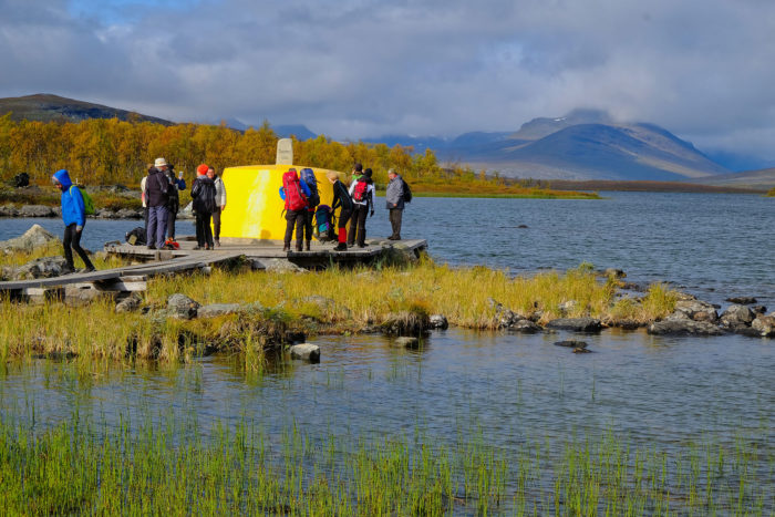A group of hikers board a yellow boat on a lake.