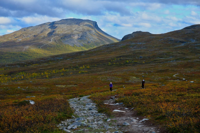 Hikers walk along a trail with a mountain in the background.