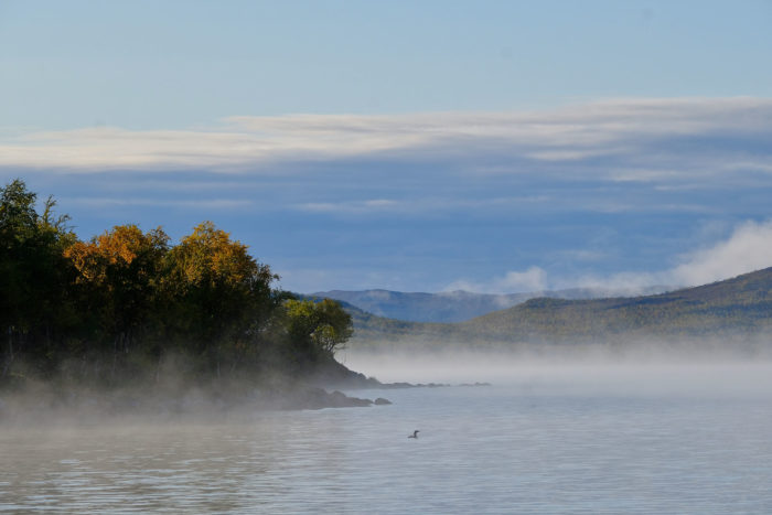 Mist rises off a lake with mountains in the background.