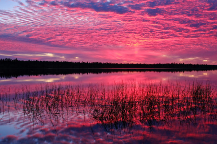 The sunset is reflected as pink colours in a lake and in clouds.