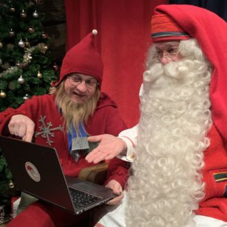 Santa Claus and an elf look intently at the screen of a laptop.