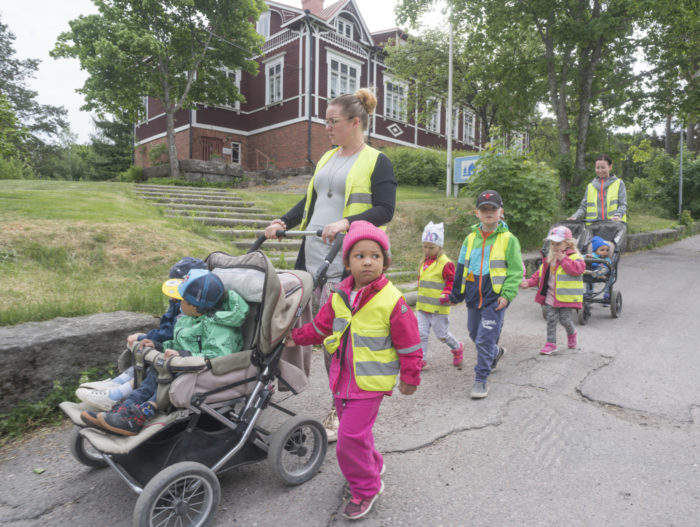 A group of daycare kids walking down the street in reflective vests with their caretaker
