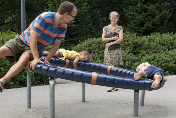 A family of four at the playground. The father plays with the two children