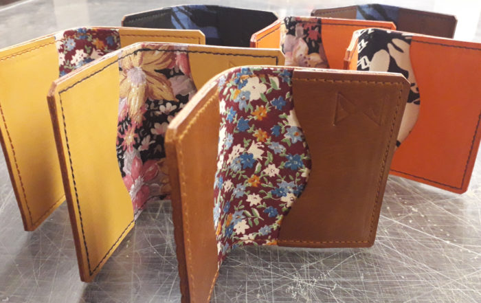 Meia dúzia de carteiras de couro estão espalhadas, equilibradas como livros abertos. Cada carteira tem um padrão de cores diferente sendo exibido dentro.