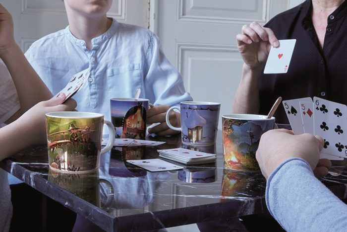 Vier Leute sitzen an einem Tisch und spielen Karten und jeder hat einen anderen Mumin-Becher vor sich.