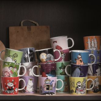 A shelf that has some wooden chopping boards, and piles of mugs with pictures of Moomin characters.