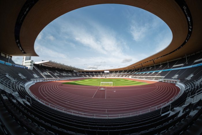 Die Innenansicht eines Stadions zeigt das Spielfeld und den Himmel, der sich über den Kanten eines Daches, das die Tribünen bedeckt, breitmacht.