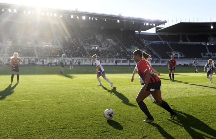 Jogadoras correm pelo campo em uma partida de futebol feminino em um estádio.