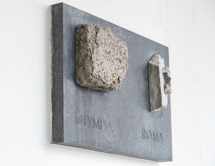 Two chunks of stone are mounted on a plaque on a wall.