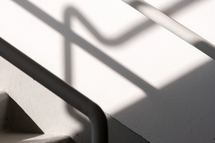 Long thin shadows fall from metal railings across a white space.