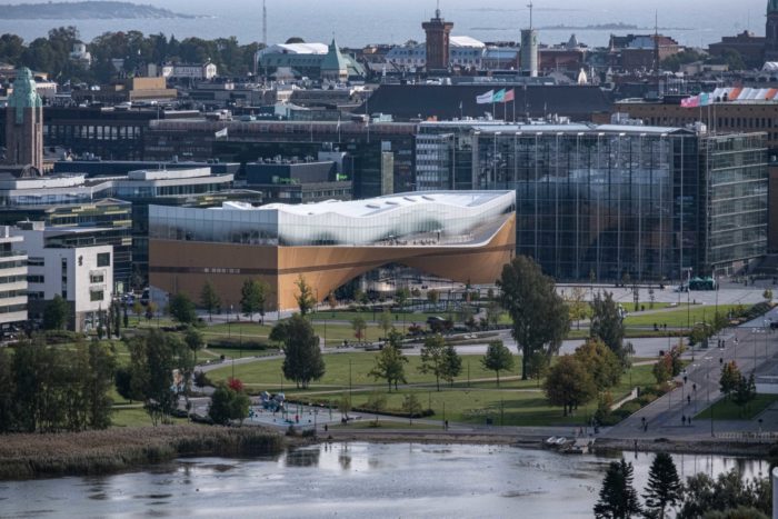 Ein Blick über Helsinki zeigt eine Bucht und ein großes Bibliotheksgebäude mit einer geschwungenen Dachkontur.