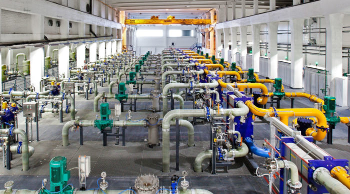 Комплекс серых, желтых и синих труб простирается на всю длину промышленного зала.