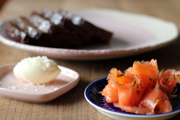 Um prato de pão fatiado, um prato de manteiga e um prato de salmão fatiado estão dispostos sobre uma mesa.