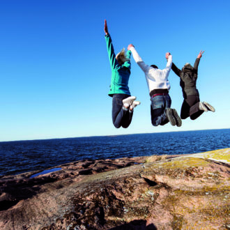 Три человека прыгают на скале на берегу моря.