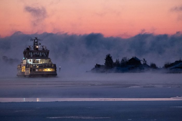 A ship progresses past the silhouette of a rocky island.