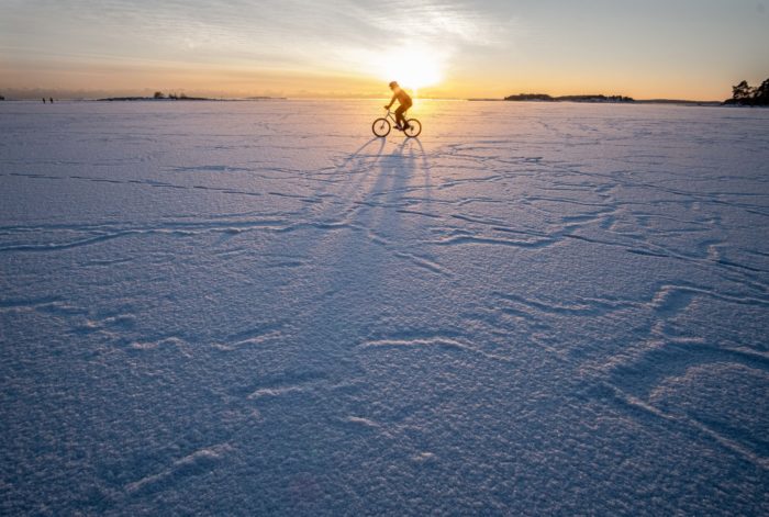 A cyclist traverses a wide, flat expanse of snow.