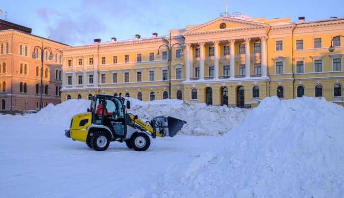 Uma máquina de terraplenagem empilha neve em montes na frente de um prédio do governo.