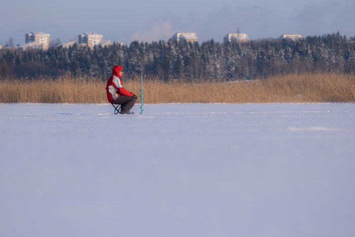 Une personne est assise sur un tabouret au milieu d’une baie pétrifiée par le gel tandis qu’on aperçoit des immeubles à l’arrière-plan.