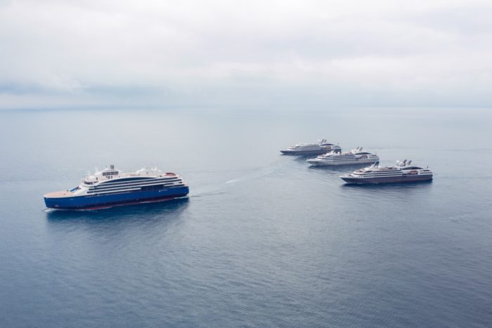 Um grande navio de cruzeiro e três ligeiramente menores navegam em águas calmas.