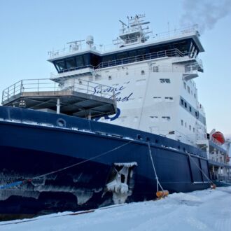A blue and white ship rests in front of an ice-covered sea.