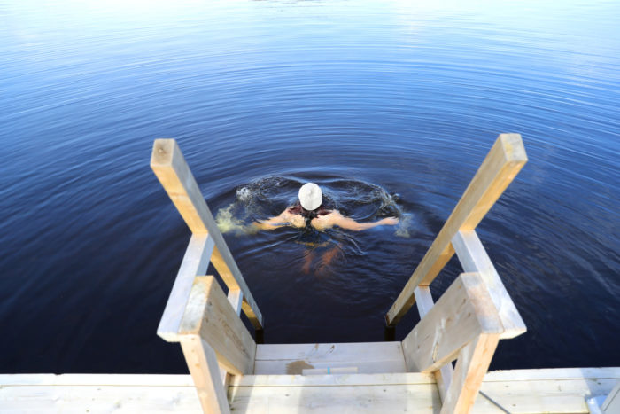 A woman is swimming in front of a wooden dock.