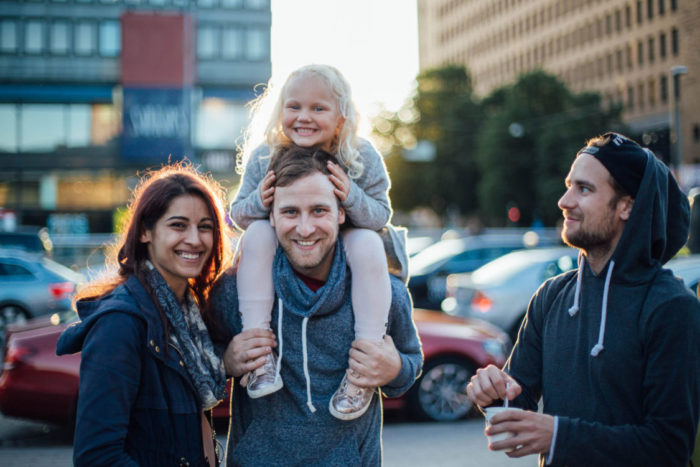Três adultos e uma menina sorriem para a câmera na frente de alguns edifícios no centro de Helsinque.