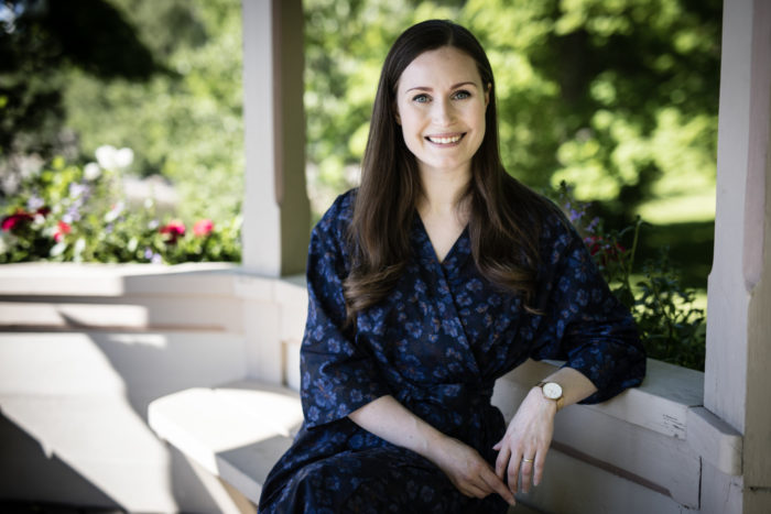 A woman is sitting on a porch, green trees visible behind her.