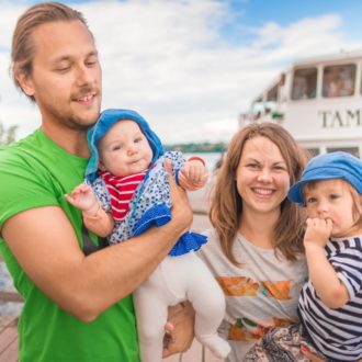 Um homem, um bebê, uma mulher e uma criança pequena estão em uma doca de balsa em um dia de verão.