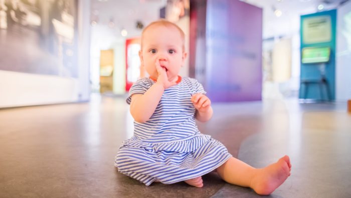 A baby sits on the floor at a museum.