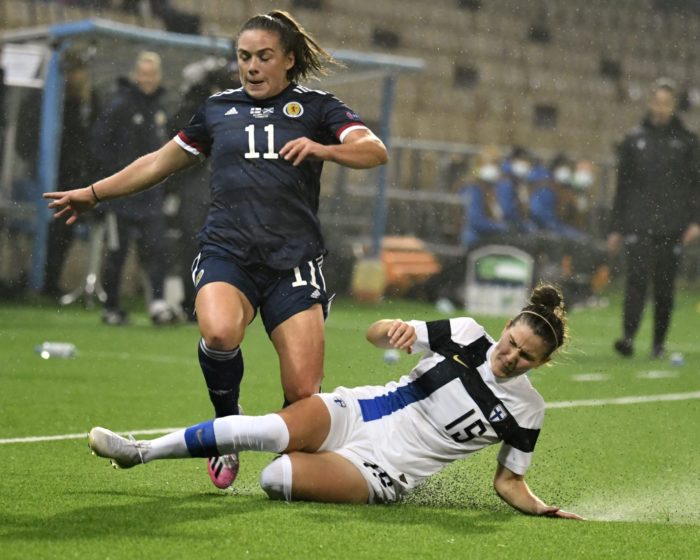 Une footballeuse finlandaise fait un tacle glissé devant une joueuse écossaise.