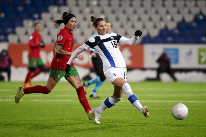 Une footballeuse finlandaise donne un coup de pied dans le ballon en étant suivie de près par une joueuse portugaise.