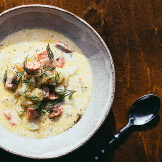 Un plato de sopa de pescado, una taza y una cuchara sobre una mesa de madera.