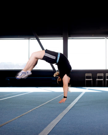 Eine Frau führt Gymnastikbewegungen in einer Sporthalle aus.