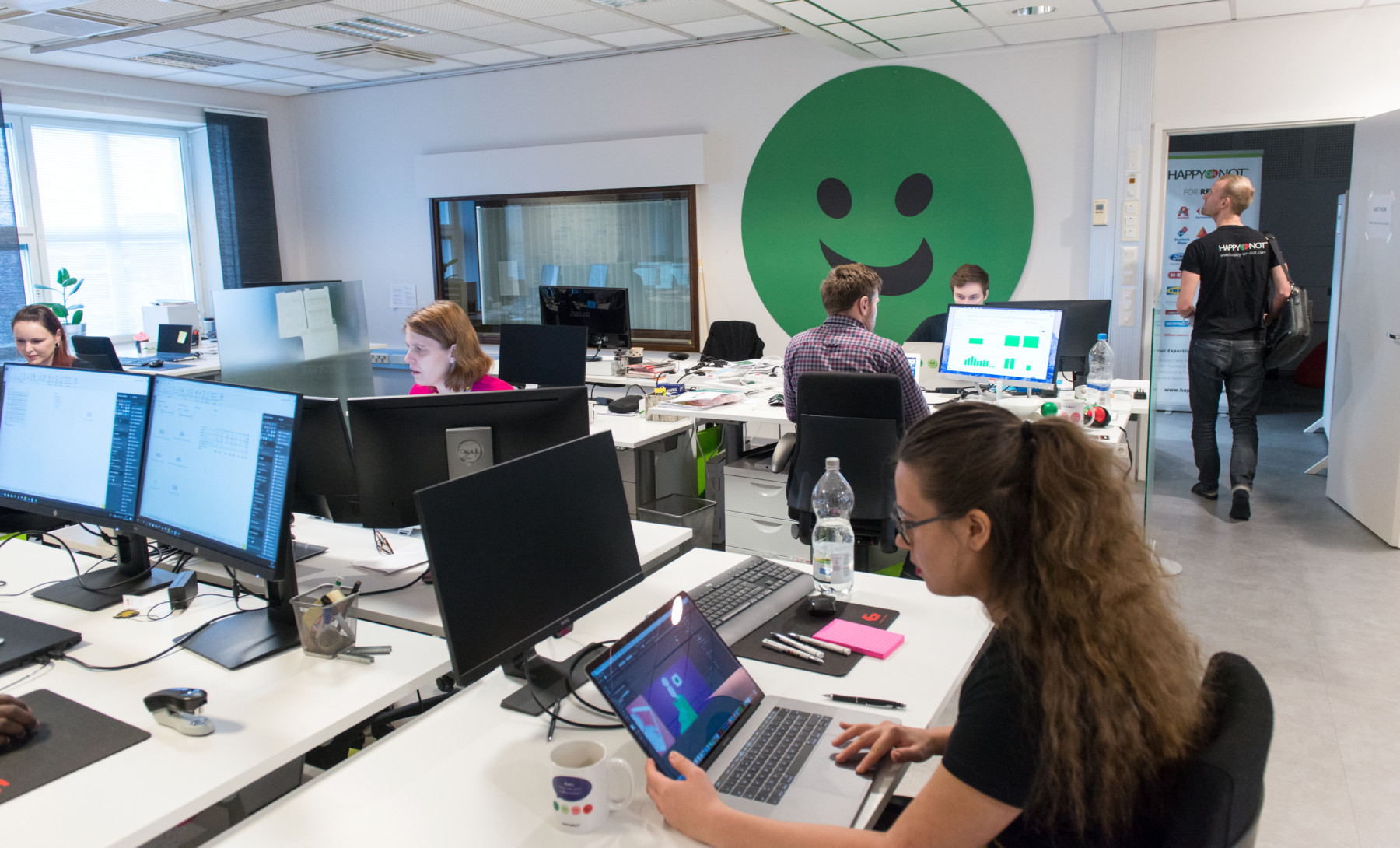 Varias mujeres y un hombre trabajan sentados ante sus ordenadores en una oficina luminosa y moderna.