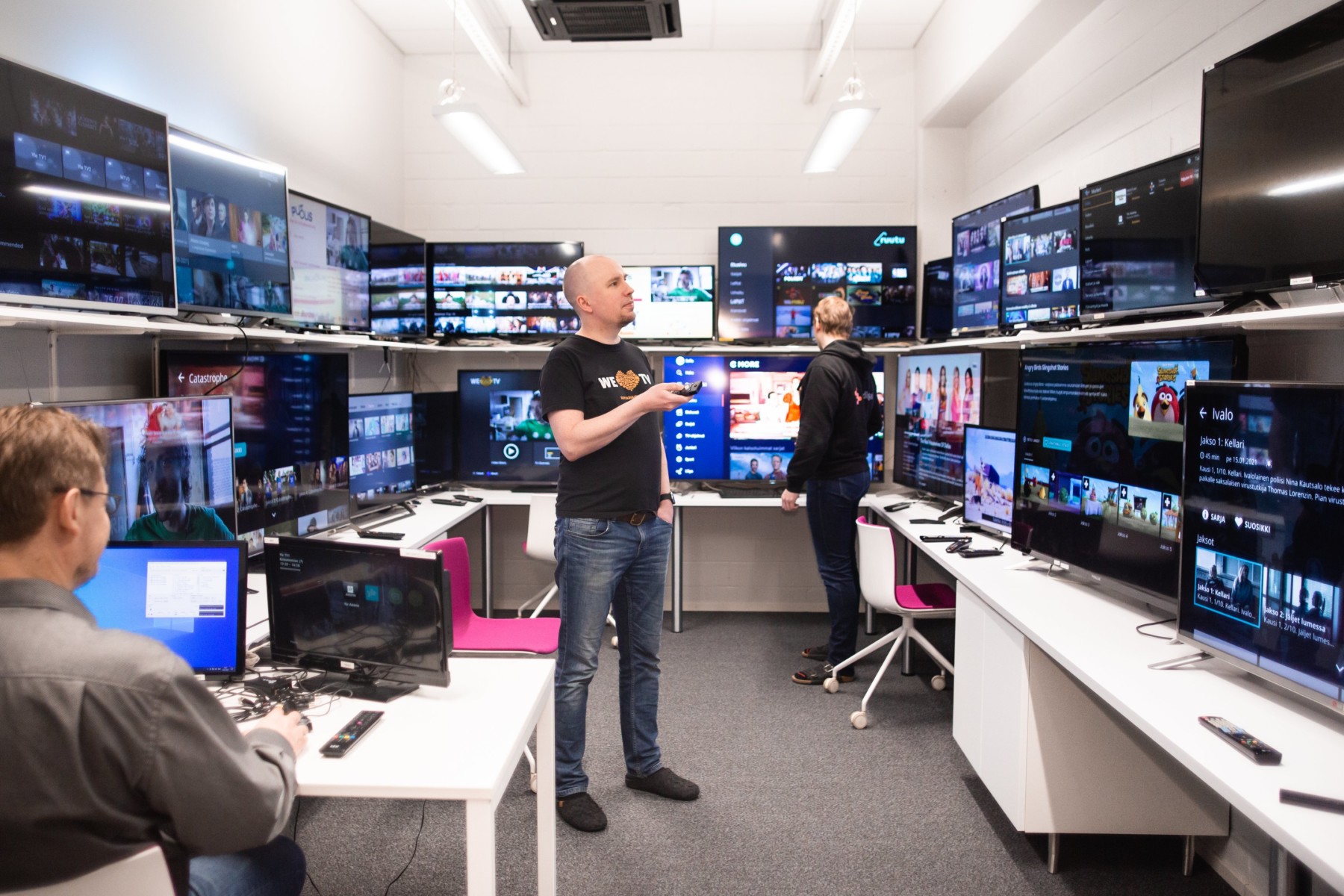 Tres hombres trabajan en una sala llena de estanterías con pantallas de televisión.