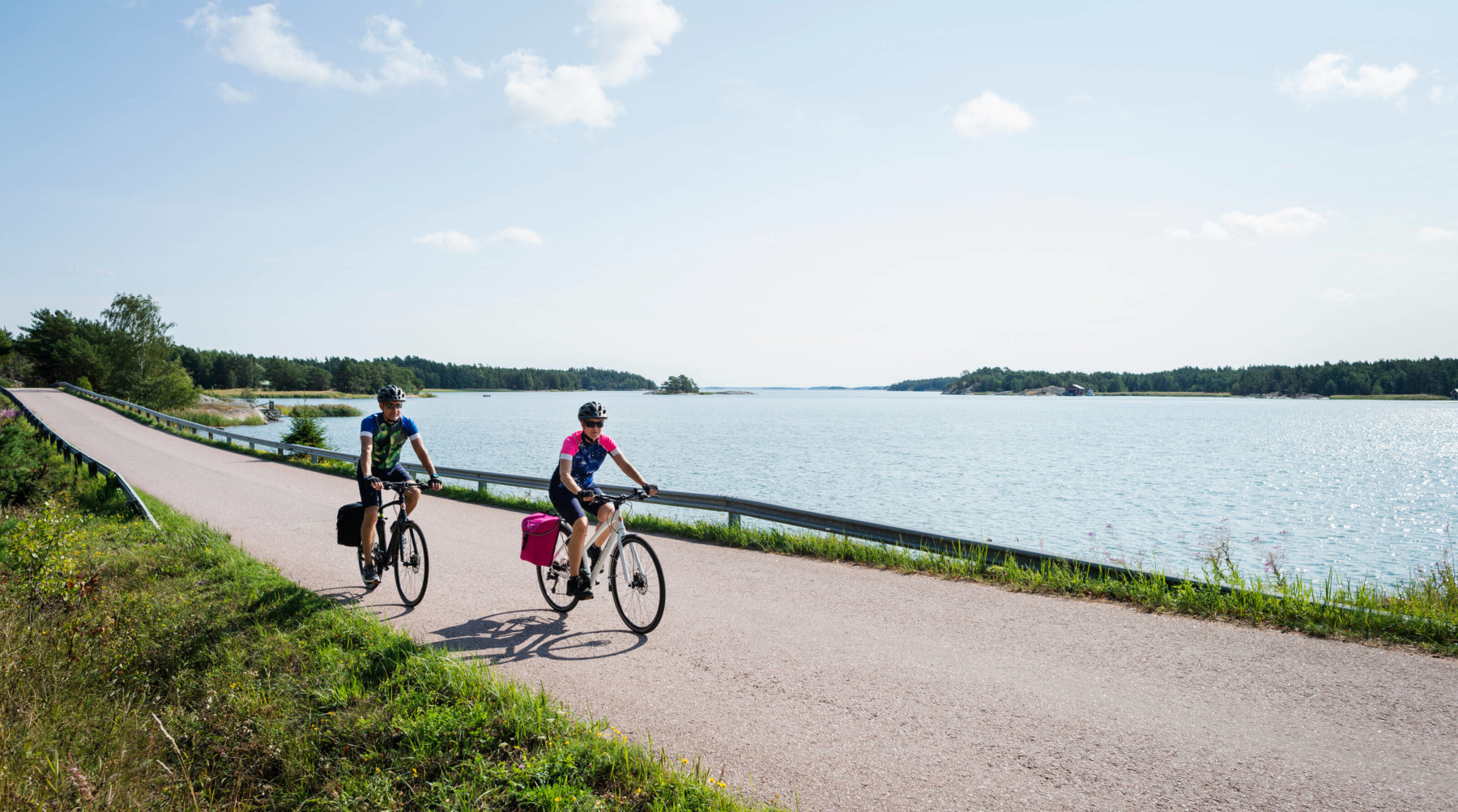 Deux personnes se déplacent en vélo sur une petite route côtière.