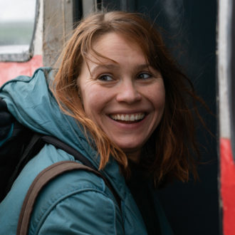 A woman wearing a jacket and a backpack smiles.